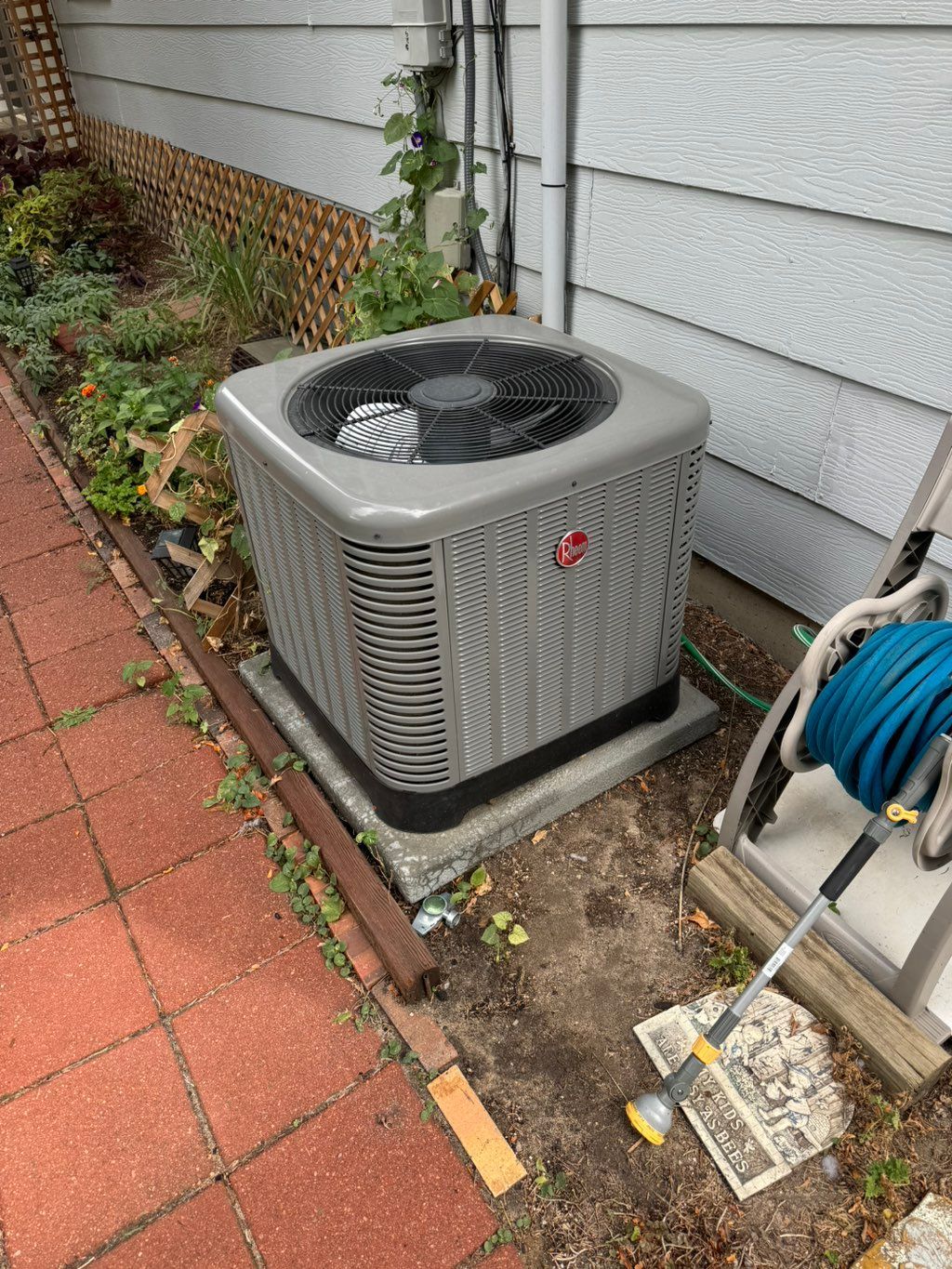 A Rheem central air conditioning condenser installed on a level pad beside a home by Temperature Select Air.